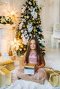 Little child sitting on floor near christmas tree, holding gift box Royalty Free Stock Photo