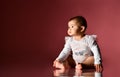 Little child in smart white bodysuit with inscription, barefoot. She smiling, sitting on floor against pink background. Close up Royalty Free Stock Photo