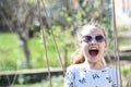 Little child smile on swing in summer yard. Fashion girl in sunglasses enjoy swinging on sunny day. Beauty kid smiling on playgrou Royalty Free Stock Photo