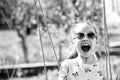 Little child smile on swing in summer yard. Fashion girl in sunglasses enjoy swinging on sunny day. Beauty kid smiling