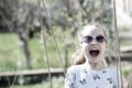 Little child smile on swing in summer yard. Fashion girl in sunglasses enjoy swinging on sunny day. Beauty kid smiling