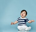 Little child in striped t-shirt, white pants and booties. He is looking up, sitting on floor against blue background. Close up Royalty Free Stock Photo