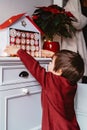 Little child taking handmade advent calendar made from toilet paper rolls.