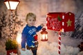 Little child, toddler boy, sending letter to santa in christmas mailbox, christmas decoration around him, outdoor snow shot Royalty Free Stock Photo