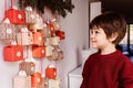 Little child waiting to start opening handmade advent calendar hanging on wall.