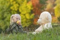 Little child on walk on autumn day in nature. Blonde girl eats apple and plays with large teddy bear sitting on grass Royalty Free Stock Photo