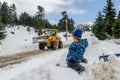 Little Child Watches the Tractor Moving Snow and Clearing the Road that Passes Through the Forest