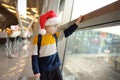 Little child wearing Santa Claus hat on background of an international airport. Preschooler boy is waiting for a merry Christmas.