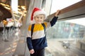 Little child wearing Santa Claus hat on background of an international airport. Preschooler boy is waiting for a merry Christmas