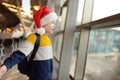 Little child wearing Santa Claus hat on background of an international airport. Preschooler boy is waiting for a merry Christmas