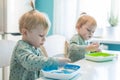 Little children blonde boys twins in pajamas hungry eating healthy food in kitchen at home