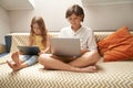 Little children, cute brother and sister sitting on sofa and using laptop and digital tablet, watching cartoons or Royalty Free Stock Photo