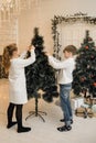 Little children decorate the Christmas tree in a bright interior. Girl and boy, brother and sister hang New Year`s toys