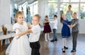 Little children in elegant dresses practicing waltz dance in school hall