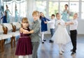 Little children in elegant dresses practicing waltz dance in school hall