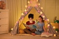 Little children with flashlight reading book in play tent Royalty Free Stock Photo