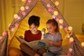 Little children with flashlight reading book in play tent Royalty Free Stock Photo