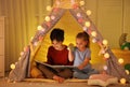 Little children with flashlight reading book in play tent