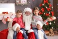 Little children with gift boxes sitting on Santa Claus` knees indoors Royalty Free Stock Photo