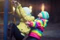 Little children play in playground in evening in park on background of shining lights.