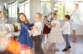 Little children practicing waltz dance in school-hall decorated with Christmas-tree