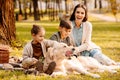 Little children and their mom sitting on a picnic blanket in a park and petting Royalty Free Stock Photo