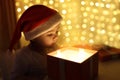 Little Christmas girl in a Santa hat looks into a magic gift box. Background color of the defocus. The concept of Royalty Free Stock Photo
