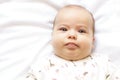 Little chubby newborn baby in a white bodysuit lying on the bed. Top view of a sad newborn baby on a white warm blanket. Royalty Free Stock Photo