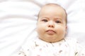 Little chubby newborn baby in a white bodysuit lying on the bed. Top view of a sad newborn baby on a white warm blanket Royalty Free Stock Photo