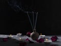 Small jug and incenses in it, decorative petals and candles on the grey table against dark wall. Calm andpiece atmosphere