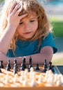 Little clever boy thinking about chess. Little boy playing chess outdoor in park. Close up face of clever smart child.