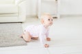 Little crawling baby girl one year old crawling on floor in bright light living room smiling and laughing. Happy toddler