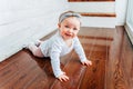 Little crawling baby girl one year old siting on floor in bright light living room near window smiling and laughing