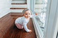 Little crawling baby girl one year old siting on floor in bright light living room near window smiling and laughing