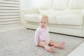 Little crawling baby girl one year old sitting on floor in bright light living room smiling and laughing. Happy toddler