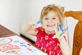 Little creative toddler girl painting with finger colors a fish. Active child having fun with drawing at home, in Royalty Free Stock Photo