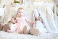 Little crying girl sitting between toy rabbits near bed