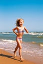 Little curly cheerful girl runs along the shore of the ocean