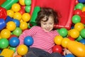 Little curly cute smile girl plays in balls for a dry pool. Play room. Happiness