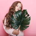 Little curly girl child wearing pink outfit and holding big green leaf Royalty Free Stock Photo