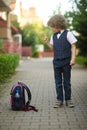 Little curly-haired schoolboy put his backpack on the sidewalk.