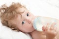 Little curly-headed baby sucks a bottle of milk Royalty Free Stock Photo