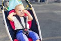 Little cute adorable toddler kid boy rubbing eyes with hands sitting in stroller on bright summer day outdoors. Tired Royalty Free Stock Photo