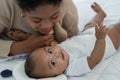 Little cute African American newborn baby lying on bed and looking smiling at camera while young mother is looking at infant Royalty Free Stock Photo