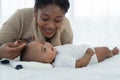 Little cute African American newborn baby lying on bed and looking smiling at young mother who is touching infant`s head with love Royalty Free Stock Photo