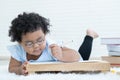 Little cute African Asian chubby kid girl wear eyeglasses learning writing on paper and lying down on fluffy carpet at home Royalty Free Stock Photo