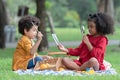 Little cute African children boy and girl sitting and have fun playing magnifying glass to read book while picnic at park together Royalty Free Stock Photo