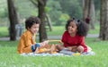Little cute African children boy and girl sitting laughing and have fun playing magnifying glass while picnic at park together. Royalty Free Stock Photo