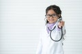 Little cute Asian child girl doctor wear medical uniform and glasses, holding stethoscope playing doctor, smiling friendly, look Royalty Free Stock Photo