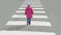 Little cute baby girl dressed in red jacket,  blue jeans and hat crosses the road at pedestrian crossing on cold day. Top view Royalty Free Stock Photo